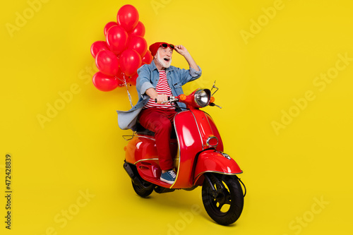 Portrait of elderly retired pensioner trendy cheerful man riding moped store open isolated over vivid yellow color background