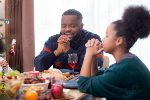 Happy African family holding hands and praying dinner on thanksgiving eve day together, merry Christmas, celebration and festive on food table, relationship of family, indoor, new year and xmas.