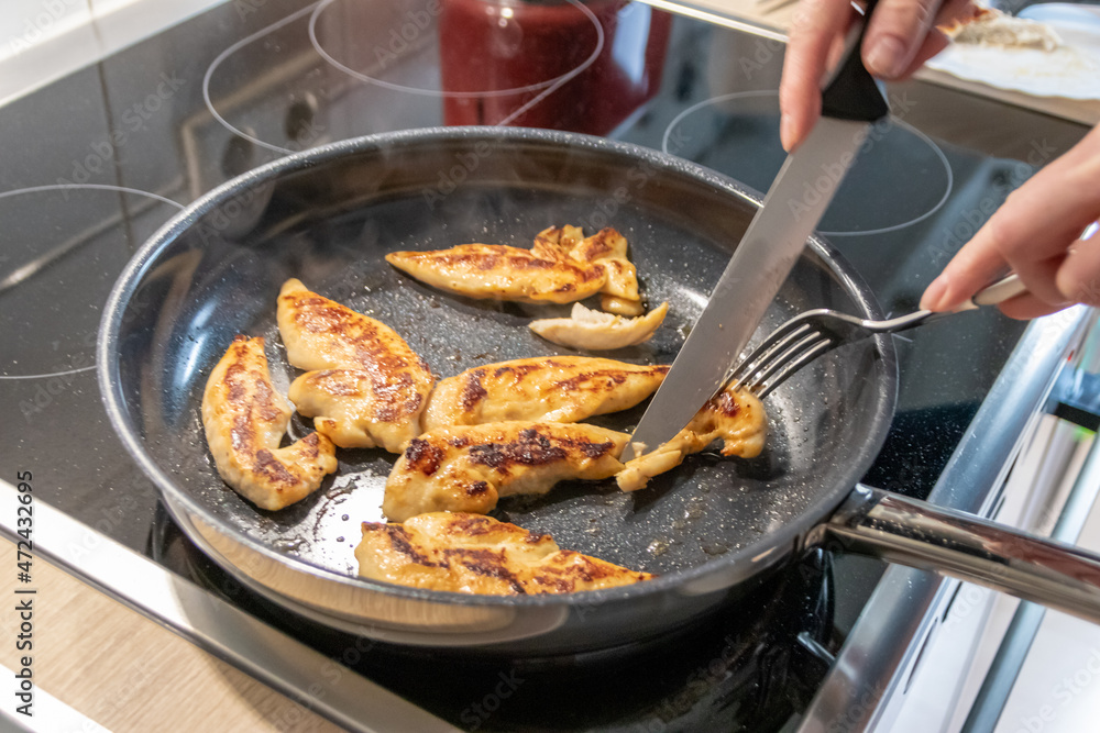 Woman cooking and frying chicken breasts and chicken filet in a pan on an hot stove in the kitchen as delicious meal and diet dinner cuisine for healthy nutrition with smoking hot meat and barbecue Woman cooking and frying chicken breasts and chicken filet in a pan on an hot stove in the kitchen as delicious meal and diet dinner cuisine for healthy nutrition with smoking hot meat and barbecue