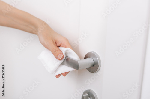 Cleaning door handles with an antiseptic wet wipe and gloves. Sanitize surfaces prevention in hospital and public spaces against corona virus. Woman hand using towel for cleaning home room door link