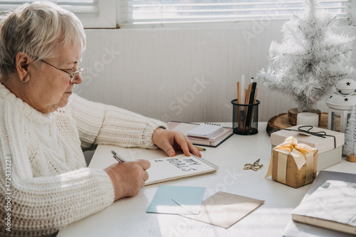 Healthy New Years resolutions for older adults. Senior mature old woman in white sweater writing handwritten text My Goals in open notepad on the table. Planning and setting goals photo