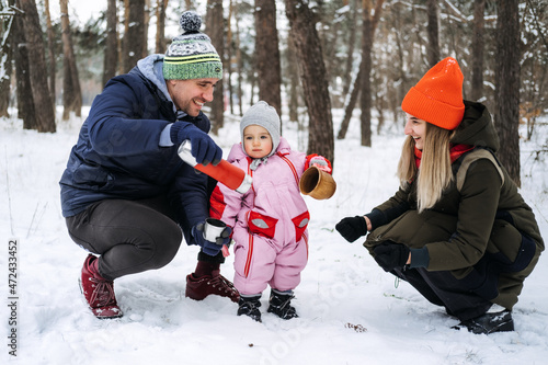 Outdoor family activities for happy winter holidays. Happy father and mother playing with little baby toddler girl daughter in winter park  forest. Happy family on winter weekend  Christmas holidays