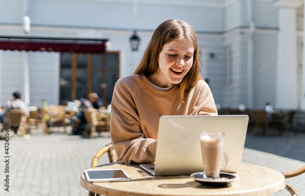A millennial woman smiles at a young hipster working on a laptop in a cafe. Breakfast at the restaurant on the street. A millennial woman smiles at a young hipster working on a laptop in a cafe. Breakfast at the restaurant on the street.
