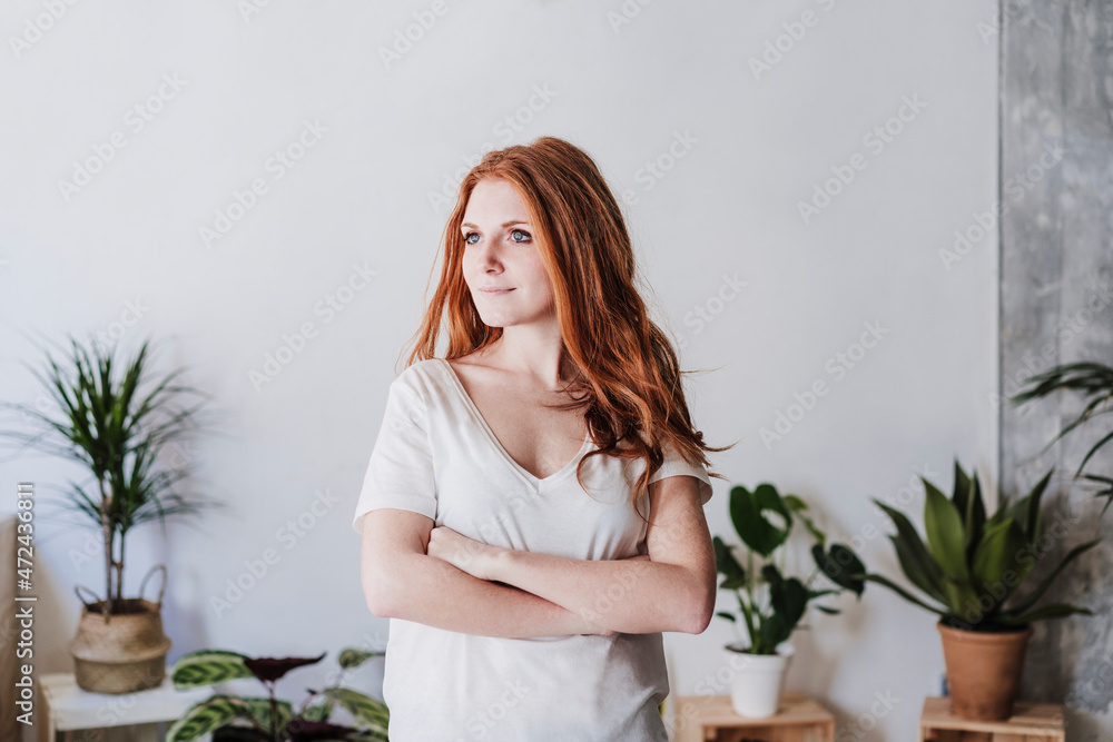 Confident woman day dreaming while standing with arms crossed in living room Confident woman day dreaming while standing with arms crossed in living room