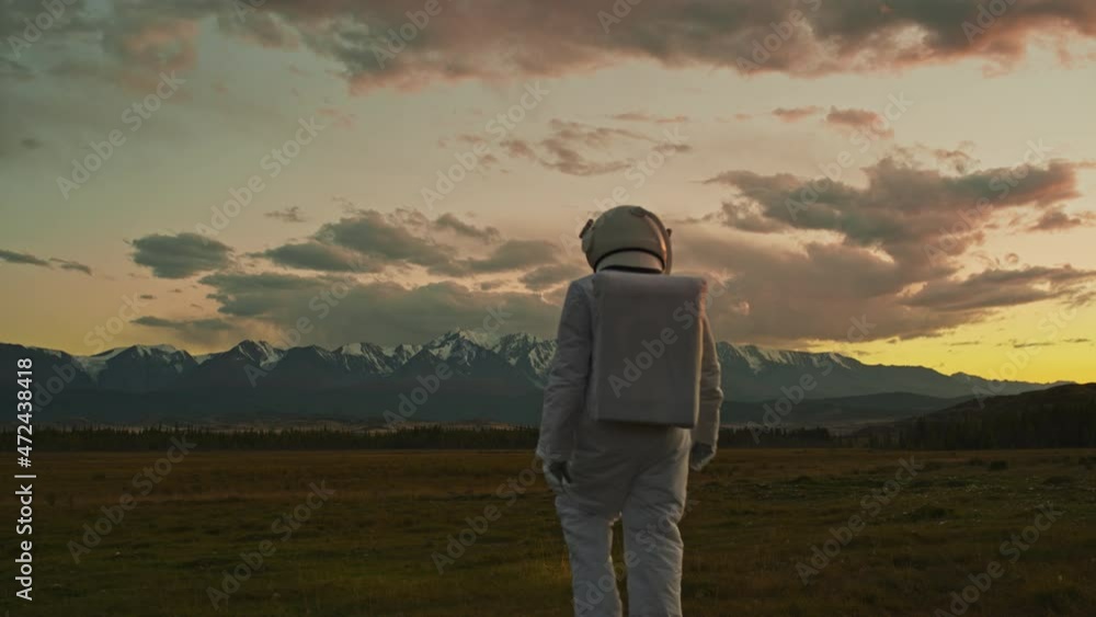An astronaut in a spacesuit explores an unknown planet. Valley with mountains in the background.