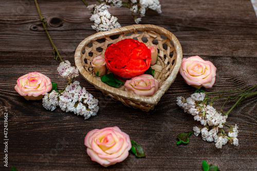 Chocolate flowers in a basket in the form of a heart. Roses, peonies on a brown wooden background.