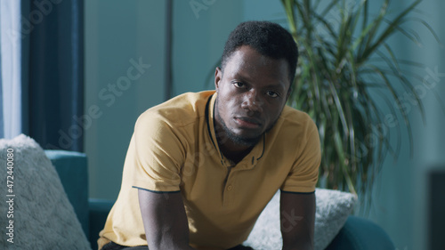 Fotografia Upset black guy looking at camera while sitting on sofa in living room at home