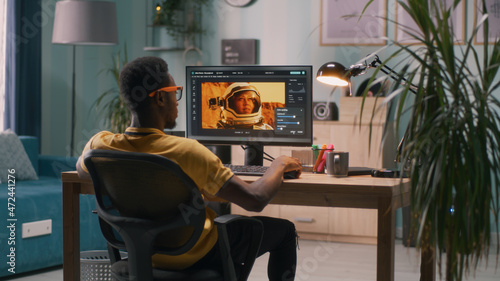 Black man using software on modern computer to edit photo in editing application of cosmonaut space man while working remotely from home photo
