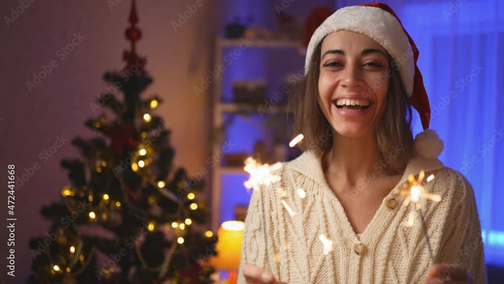 close up face happy smiling woman in Santa hat with burning sparklers at Christmas Eve or New Year at cozy house with Christmas tree. cinematic 4k slow motion close up face happy smiling woman in Santa hat with burning sparklers at Christmas Eve or New Year at cozy house with Christmas tree. cinematic 4k slow motion