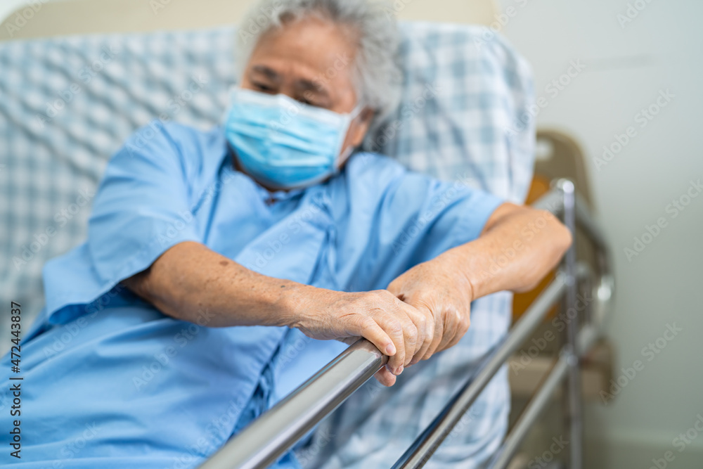 Asian senior or elderly old woman patient wearing mask for protect coronavirus lie down handle the rail bed with hope on a bed in the hospital Asian senior or elderly old woman patient wearing mask for protect coronavirus lie down handle the rail bed with hope on a bed in the hospital