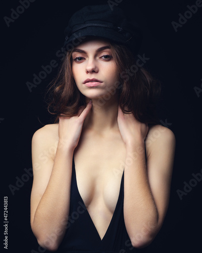 Fashionable studio portrait of a beautiful young model in black hat and sexy top on a black background. Low key.