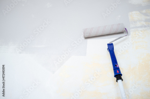 Sponge roller on a wooden stick repaints the wall gray. Home renovation. Copy space. 