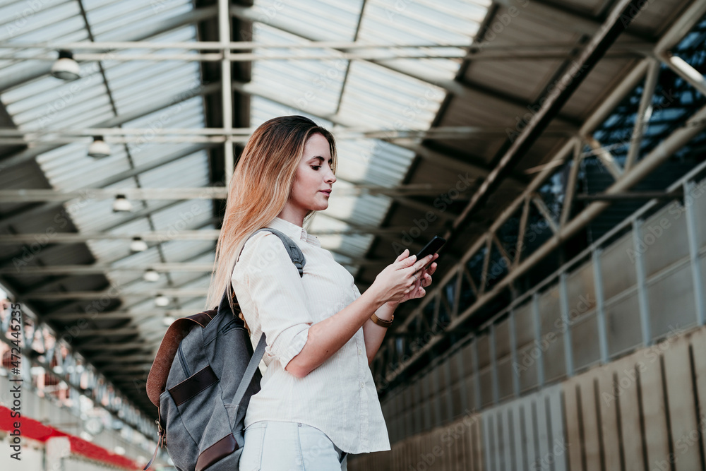 Young woman wearing backpack using smart phone at railroad station Young woman wearing backpack using smart phone at railroad station