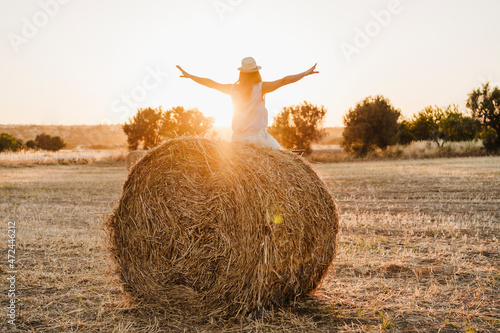 Carefree woman with arms outstretched sitting on straw bale in field