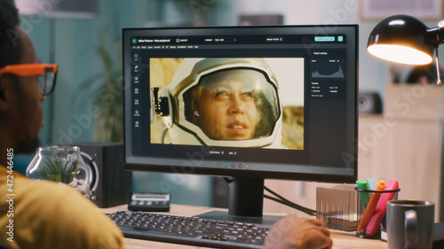 Black man using software on modern computer to edit photo in editing application of cosmonaut space man while working remotely from home