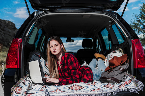 Female freelancer lying with laptop in car trunk on sunny day photo