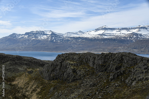 Blick über einen Fjord auf die Berge auf den Färöer Inseln, im Vordergrund schwarzes Gestein