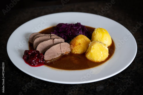 ready to eat, delicious meal from roe deer yearling with potatoes and red cabbage, brown sauce and cranberries on a white plate