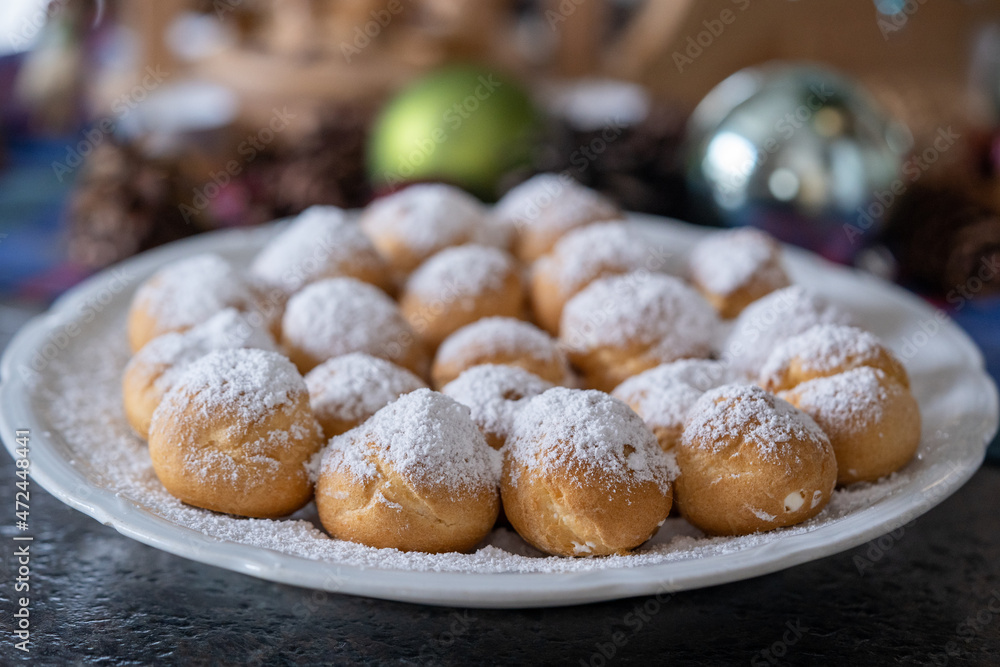 ready to eat on coffe time - small  cream puffs with powder sugar with christmas decor in the background