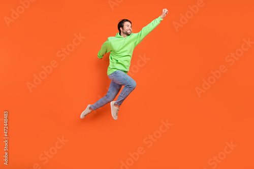 Full length photo of brunet millennial guy run save wear sweater jeans sneakers isolated on orange background