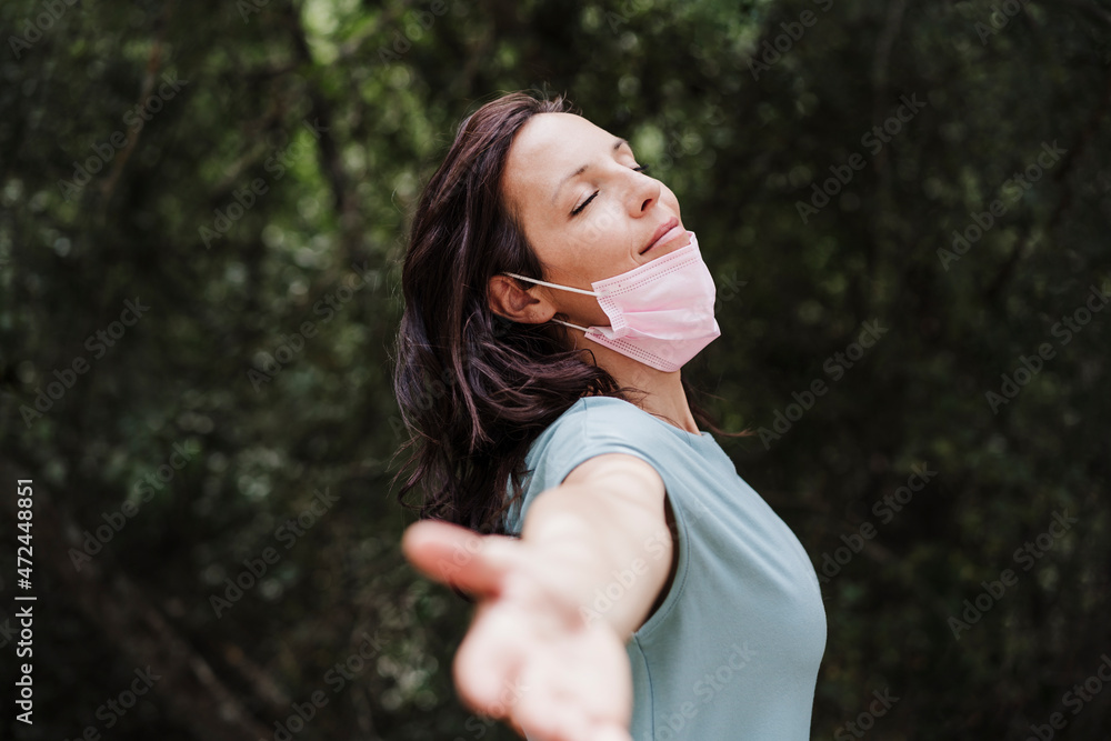 Mid adult woman standing with arm outstretched in forest during pandemic Mid adult woman standing with arm outstretched in forest during pandemic