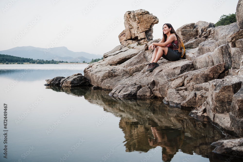 Smiling female hiker looking away while sitting on rock at lake Smiling female hiker looking away while sitting on rock at lake