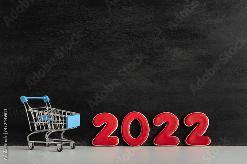 Small trolley cart and numbers 2022 on dark background. Shopping for the new year. New Years discounts.