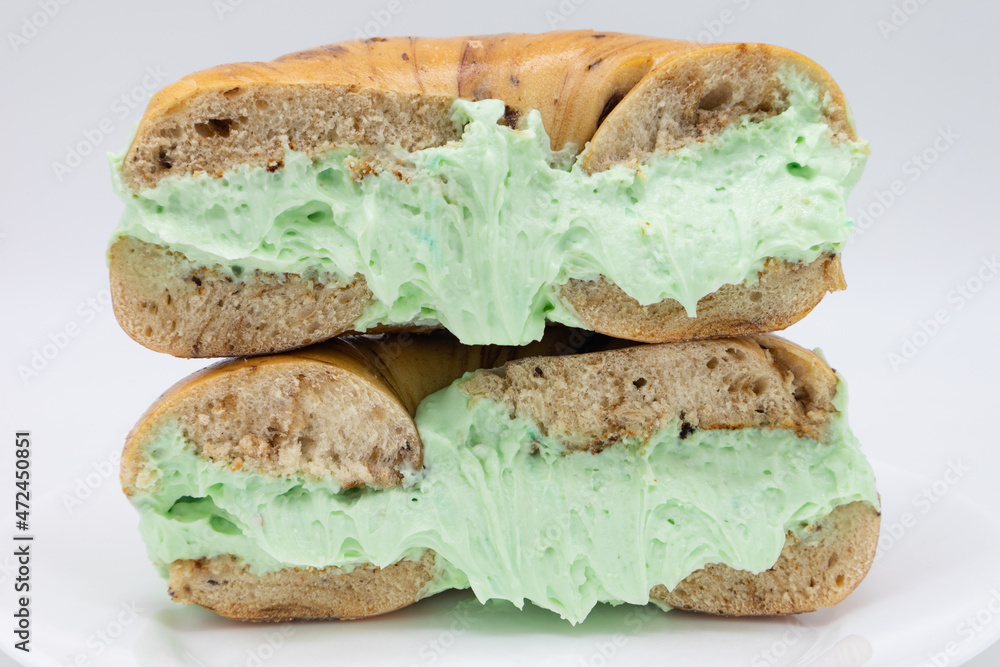 Cut In Half New York City Style Cinnamon Raisin Bagel with Pistachio Cream Cheese on a White Plate Cut In Half New York City Style Cinnamon Raisin Bagel with Pistachio Cream Cheese on a White Plate
