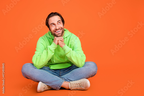Full length photo of brunet millennial man sit look promo wear green sportscloth jeans footwear isolated on orange color background © deagreez