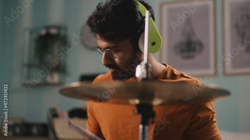 Foto Bearded Indian drummer in wireless headphones playing rhythmic tune on drums dur