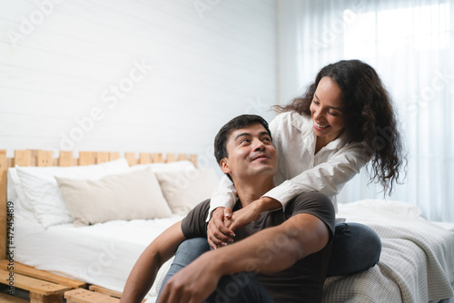 Happy young Hispanic couple sitting beside the bed talking and enjoying new home in morning