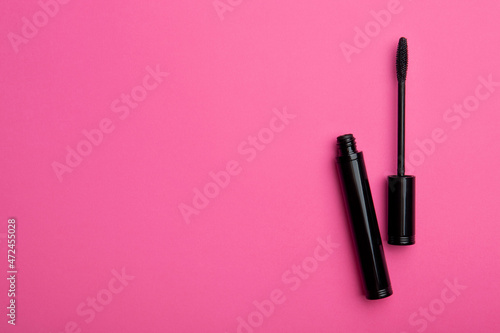 Mascara tube and brush on pink background. Unbranded mascara bottle, top view with place for text. Makeup, visage and cosmetology concept