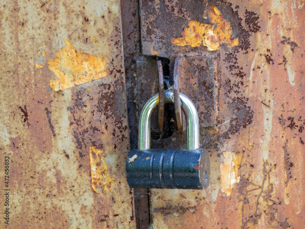 Aged damaged metal doors are padlocked. Rough rusty surface. Aged damaged metal doors are padlocked. Rough rusty surface.