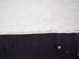 The contrasting wall is covered with white and black paint. Dirty surface with spots and cracks.