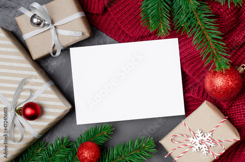 Christmas greeting card mockup with decorated gift boxes and fir tree branches on red knitted background