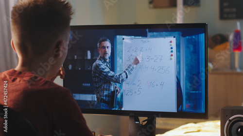 Back view of teen student listening and asking questions to math teacher during online lesson at home in daytime