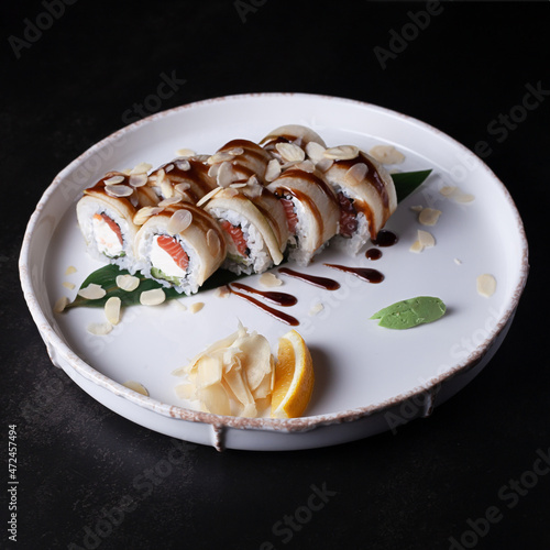 Sushi, light rolls rolls with fish and rice, on a white plate on a dark background, shot from the side