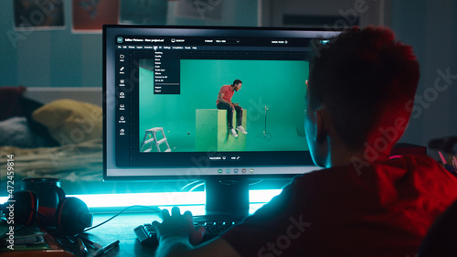 Unrecognizable teenager removing chromakey on photo and loading 3D background while learning to use editing software on computer at night at home