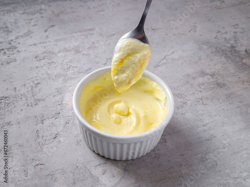 Side view of cheese sauce (coulis de parmesan) in a white bowl with a small metal spoon. Contains parmesan, cream and saffron.
