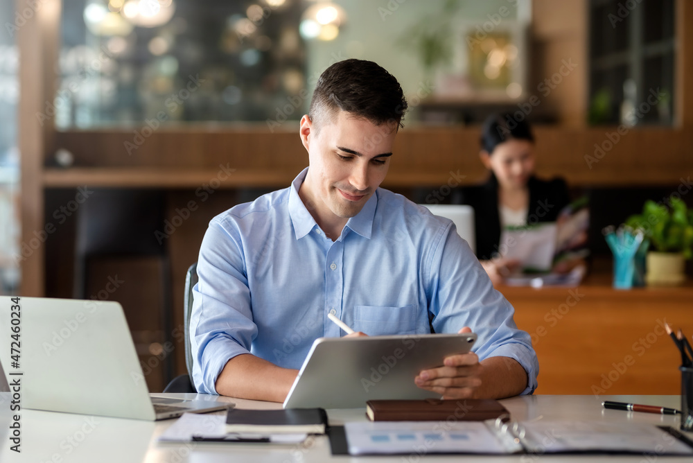 Charming businessman smiling using tablet work at the office.