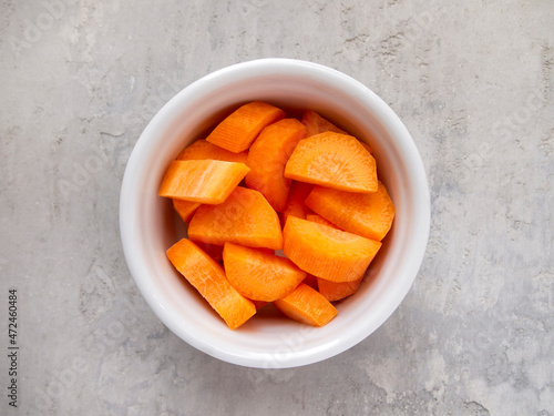 Top view of a white bowl with chopped carrots. Paysanne cut.