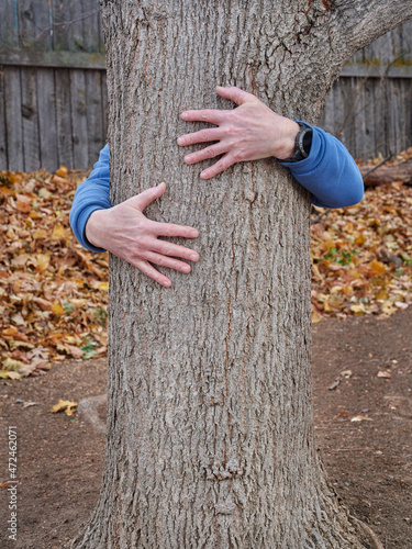 man hugging a tree in a backyard - nature connection and environment concept