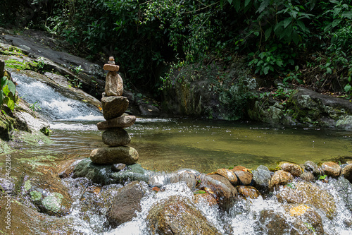 várias pedras empilhadas nas margens de uma cachoeira demonstrando a prática da meditação, 
 do equilibrio e da arte zen do balanceamento de pedras photo