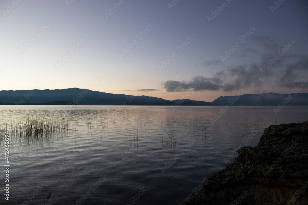 beautiful Orange and blue sunrise with calm lake, water plants and blue mountains at background
