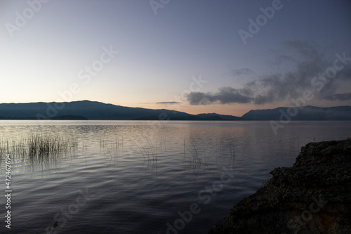beautiful Orange and blue sunrise with calm lake, water plants and blue mountains at background
