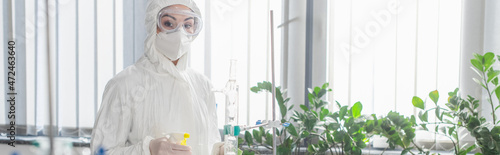 scientist in hazmat suit looking at camera while holding spray bottle, banner.