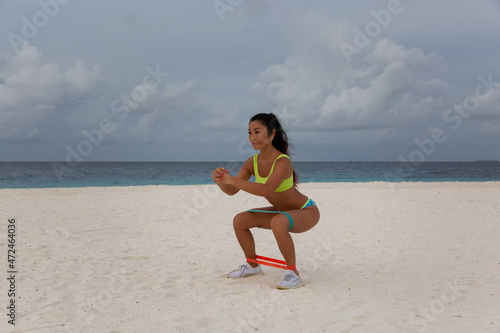 A young attractive sexy girl in a sports uniform, in a bikini, does physical exercises on the beach by the sea, at sunset. Background blue sea and cloudy sky