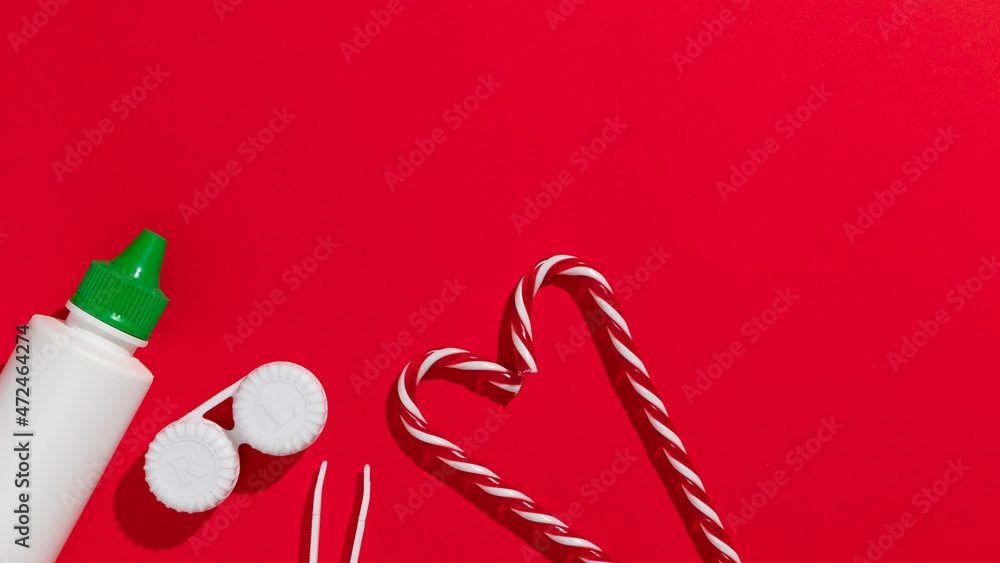 Christmas gift card with staff for spectacles correction: contact lenses, lenses tweezer and contact lens solution on the red background with candy cane Christmas gift card with staff for spectacles correction: contact lenses, lenses tweezer and contact lens solution on the red background with candy cane