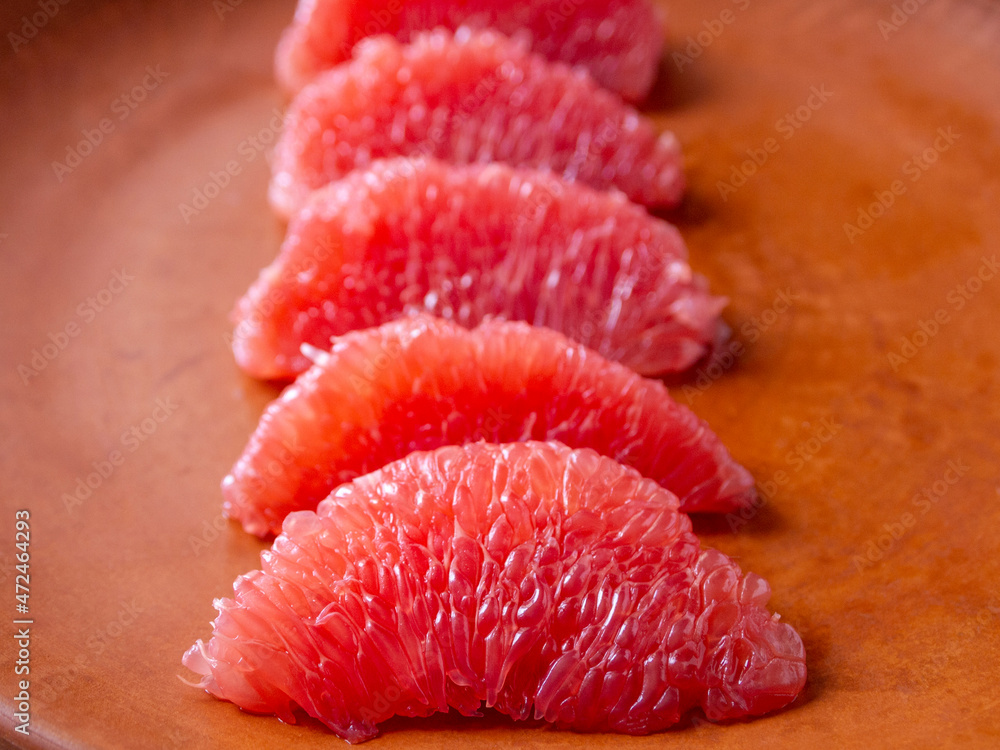Side view of peeled grapefruit slices on a brown clay plate. Side view of peeled grapefruit slices on a brown clay plate.