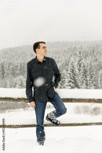 Handsome manl walks in a snowfall. Young man standing in the winter forest.Outdoor portrait of man posing in wood photo